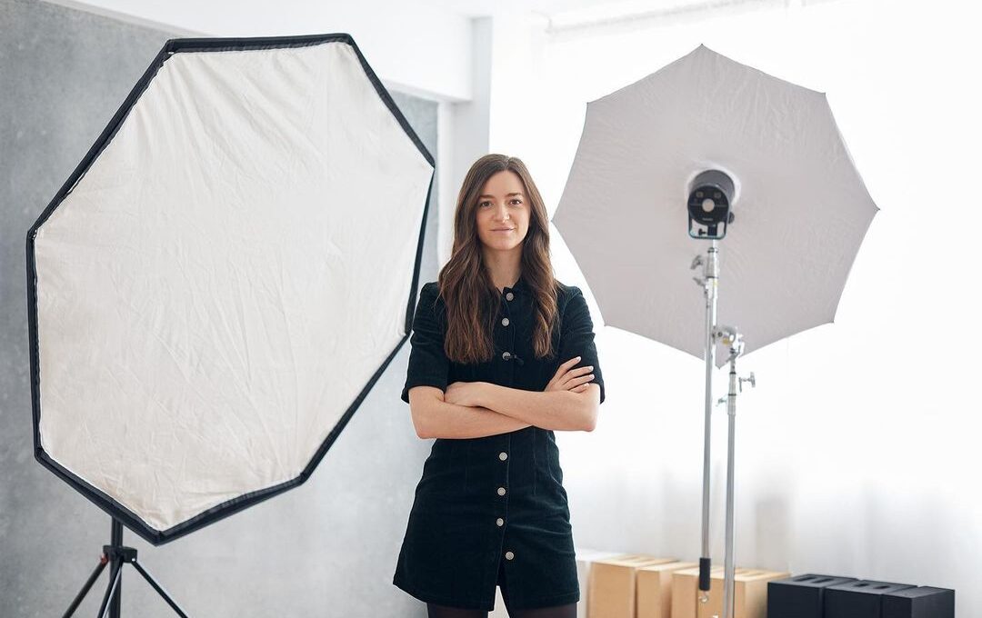 Fotógrafa joven en un estudio moderno de fotografía y vídeo, rodeada de equipos de iluminación profesional, proyectando un ambiente de trabajo creativo y técnico.